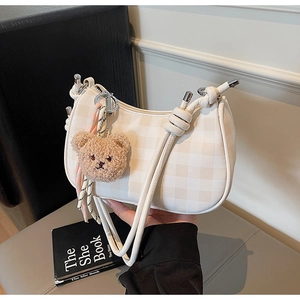 Detail of cream checkered pattern shoulder bag featuring a cute brown plush bear charm