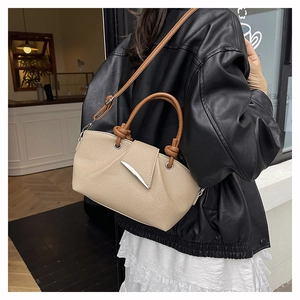Close-up of beige lychee grain leather tote with brown round handle and metal buckle