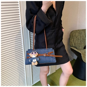 Detail of dark blue denim shoulder bag with brown leather strap and cute bear charm