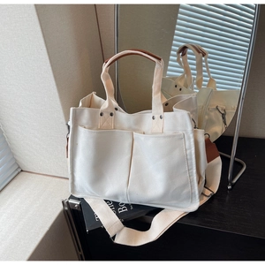 Detail view of canvas tote bag with brown leather handles and front double pockets