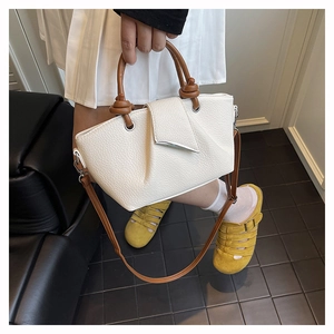 Macro view of white litchi pattern leather tote with brown knotted handle and metal trim
