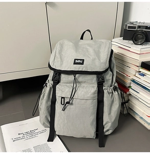 Detail of light gray nylon backpack with front DAPJ label and side drawstring pocket