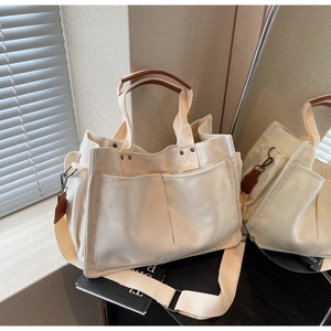 Detail of cream canvas tote bag featuring premium brown leather handles and outer pockets