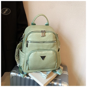 Detail of light green pebbled leather backpack with triangular logo on a silver suitcase