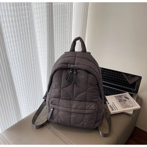 Detailed close-up of dark grey wave-quilted backpack on a leather bench in minimalist room