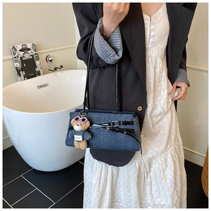 Detailed shot of a blue denim shoulder bag with leather straps and a stylish teddy bear charm
