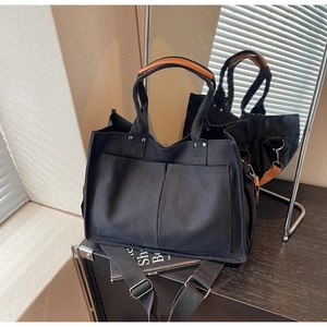 Detail of black canvas tote bag showing front pockets and brown leather handle wrap