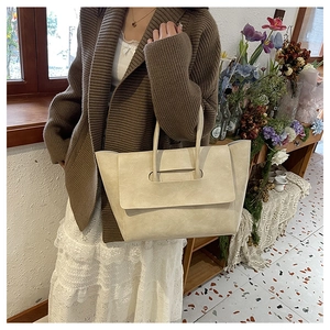 Close-up of a cream tote bag with unique flap handle design shown in a home setting