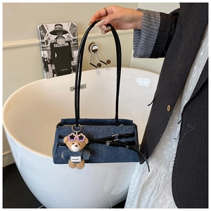 Detail of dark blue denim baguette bag with leather straps and cute bear charm accessory