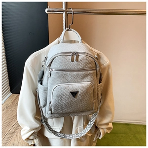 Detail of grey pebble leather backpack with triangular metal logo and woven strap