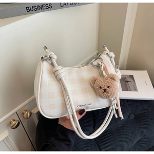 Detail of cream checkerboard underarm bag featuring a cute bear charm and knotted straps