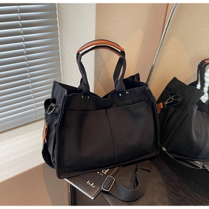 Detail of black canvas tote bag with front pockets and brown leather handle covers