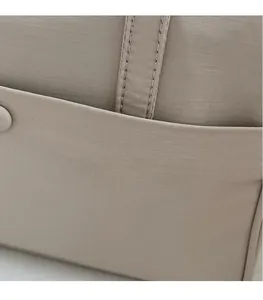 Dettaglio della borsa in tela beige con trama a quadretti e tasca esterna rinforzata