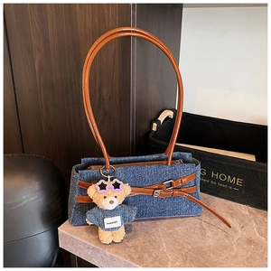 Detail of blue denim baguette bag with brown leather straps and a cute bear charm