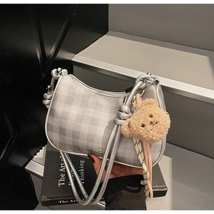 Close-up of silver plaid shoulder bag with plush bear charm and metallic texture finish