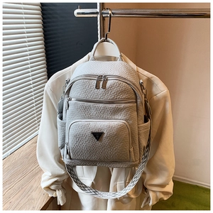 Detail of light grey multi-pocket backpack showing fabric texture and metal brand plaque