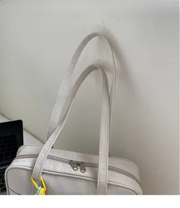 Dettaglio della borsa tote bianco sporco con tracolla lunga e decorazione a catena gialla