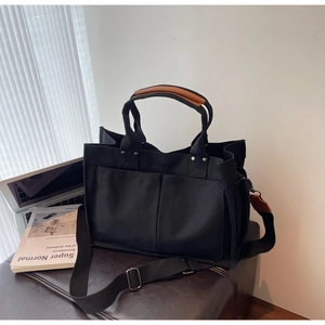 Close-up of black canvas tote bag with brown leather handles and dual front pockets