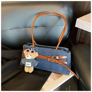 Close-up of denim shoulder bag with brown leather straps and cute plush bear charm