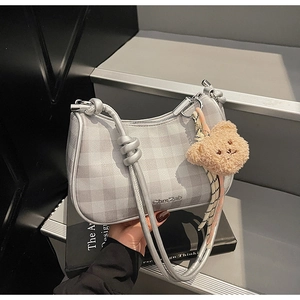 Detail of silver textured underarm bag with metal strap knots and plush bear charm