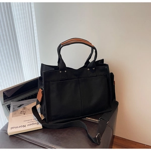 Detail of black canvas tote bag with brown leather handles and adjustable shoulder strap