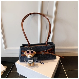 Detail of blue denim shoulder bag featuring brown leather handles and cute bear charm