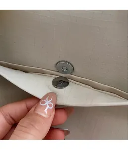 Dettaglio della fibbia magnetica argento sulla borsa in tela ripstop beige a trama fitta