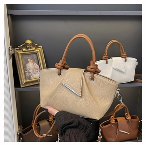 Detail of lychee pattern leather tote bag featuring knotted handle and metal accent buckle