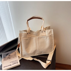 Detail view of cream canvas tote bag with front pockets on a desk with laptop