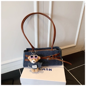 Detail of blue denim shoulder bag featuring brown leather straps and a cute teddy bear charm