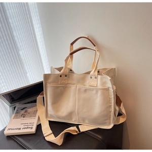 Minimalist off-white canvas tote bag detail with brown leather handles and side pockets