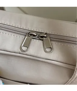 Dettaglio macro della doppia cerniera in metallo su una borsa a tracolla in tela beige