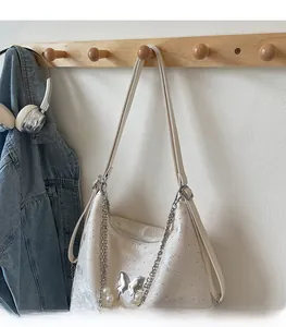 Détail d'un sac cabas blanc crème avec breloques en perles et papillon argenté sur un cintre
