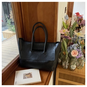 Close-up of black leather tote bag with fine texture on a sunny wooden windowsill