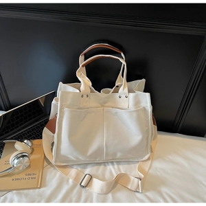 Detail of canvas tote bag with brown leather handles and adjustable shoulder strap on bed