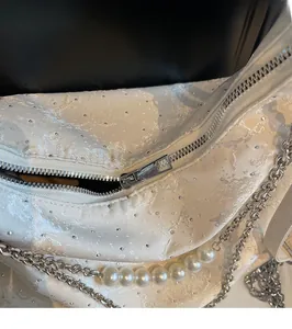 Détail de la fermeture éclair argentée et chaîne de perles sur tissu jacquard blanc