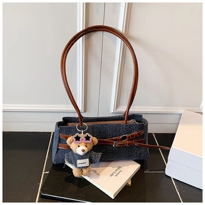 Detail of dark blue denim baguette bag with brown leather strap and cute bear charm