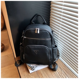 Close-up of a black pebbled leather backpack with metallic logo and wide woven straps