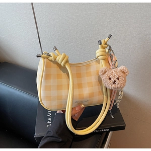 Close-up of yellow plaid shoulder bag with rope handle and plush bear charm detail