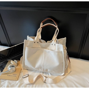 Close-up of beige canvas tote bag showing brown leather handles and spacious front pockets
