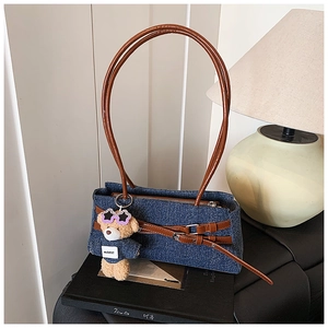 Detail of denim shoulder bag with brown leather straps and cute plush bear charm