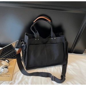 Close-up of black canvas tote bag featuring brown leather handles and silver rivet details
