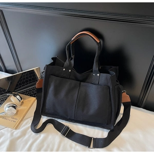 Detail of black canvas tote bag showing large front pockets and brown leather handles