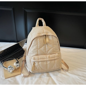 Detailed view of cream quilted backpack with laptop and travel items on a bed