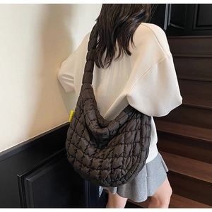 Side view of black quilted puffer hobo bag worn by model in minimalist indoor setting