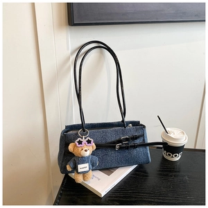 Detail of blue denim baguette bag featuring a chic bear charm and black leather strap