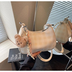 Detail of cream checkerboard underarm bag with plush bear charm and silk scarf decoration