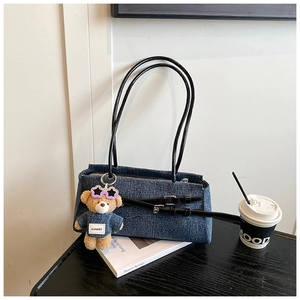Detail of dark blue denim shoulder bag with leather straps and a cute plush bear charm