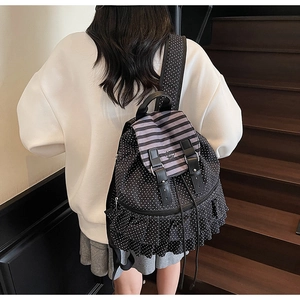 Detail of black polka dot canvas backpack with striped flap and ruffled hem on model