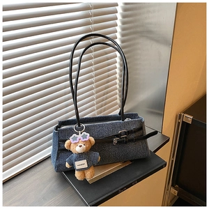 Detail of blue denim shoulder bag with leather buckles and cute plush bear charm